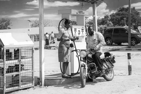 A black-and-white photo of a fuel station attendant serving a motorcycle rider at a Gilbarco fuel pump in Moroto, Uganda